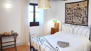Een slaapkamer met een bed, nachtkastje, lamp, raam en een wanddecoratie.