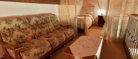 A cozy room with a floral sofa, a wooden table with a lace tablecloth, and a bed with a metal frame.