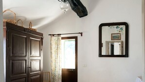 A bedroom with a large bed, a wooden wardrobe, a chair, a window with curtains, and a mirror on the wall. - Small House in the Hills for Beautiful Walks Near the Sea (Stellanello)