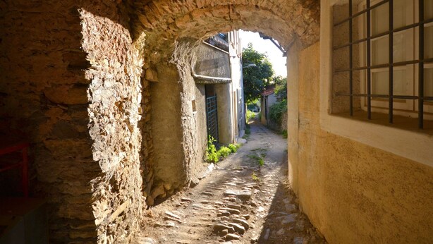 A narrow stone pathway leading through an arched doorway, flanked by rustic stone walls and a window with barred glass. - Small House in the Hills for Beautiful Walks Near the Sea (Stellanello)