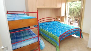 A dormitory room with bunk beds, a wooden cabinet, a small table with a lamp, and a balcony with a view of trees. - Sun Drenched Seaside Holiday Home near Venice (Rosolina)