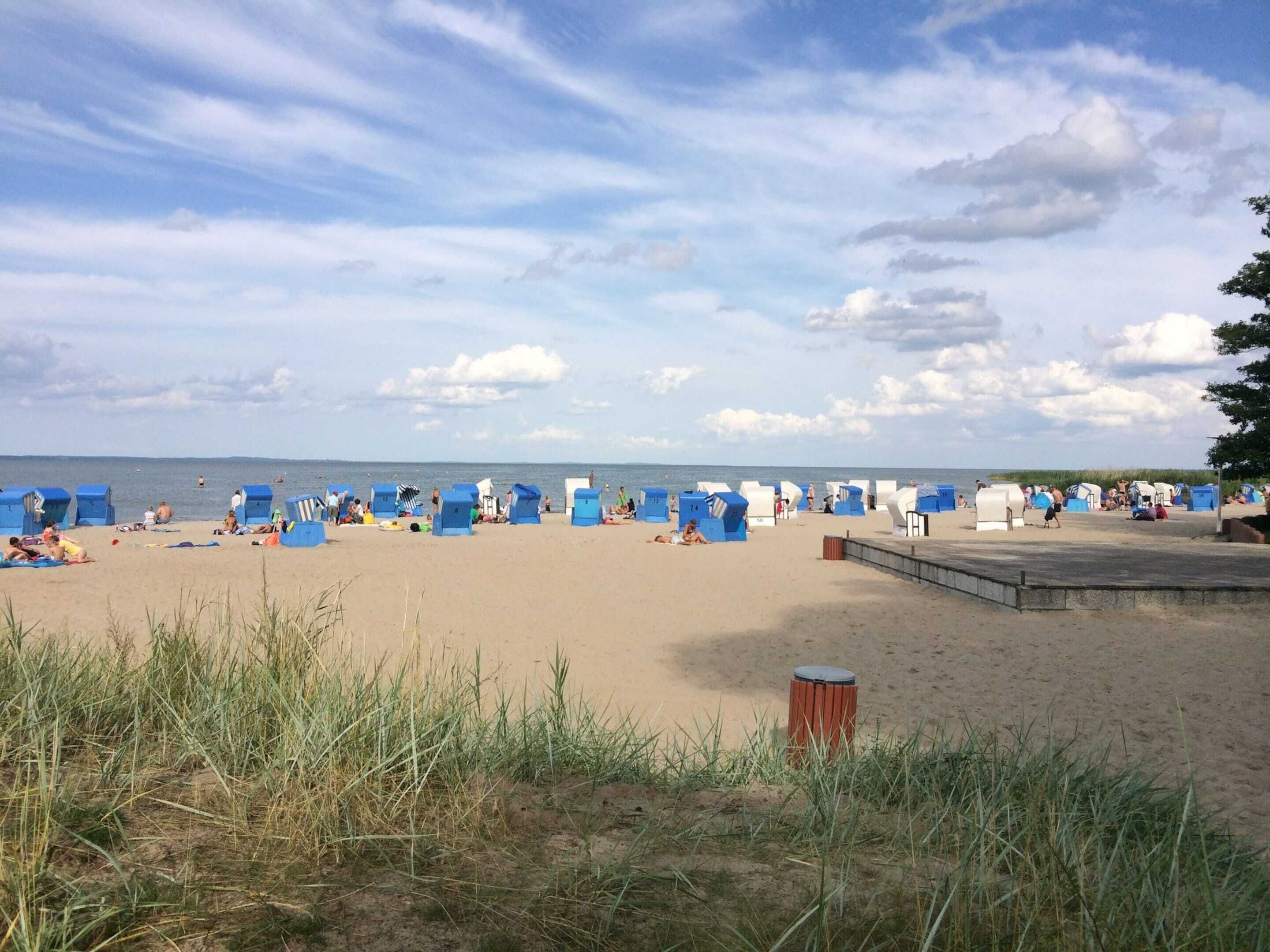 A beach with rows of blue beach huts and a sandy area with people.