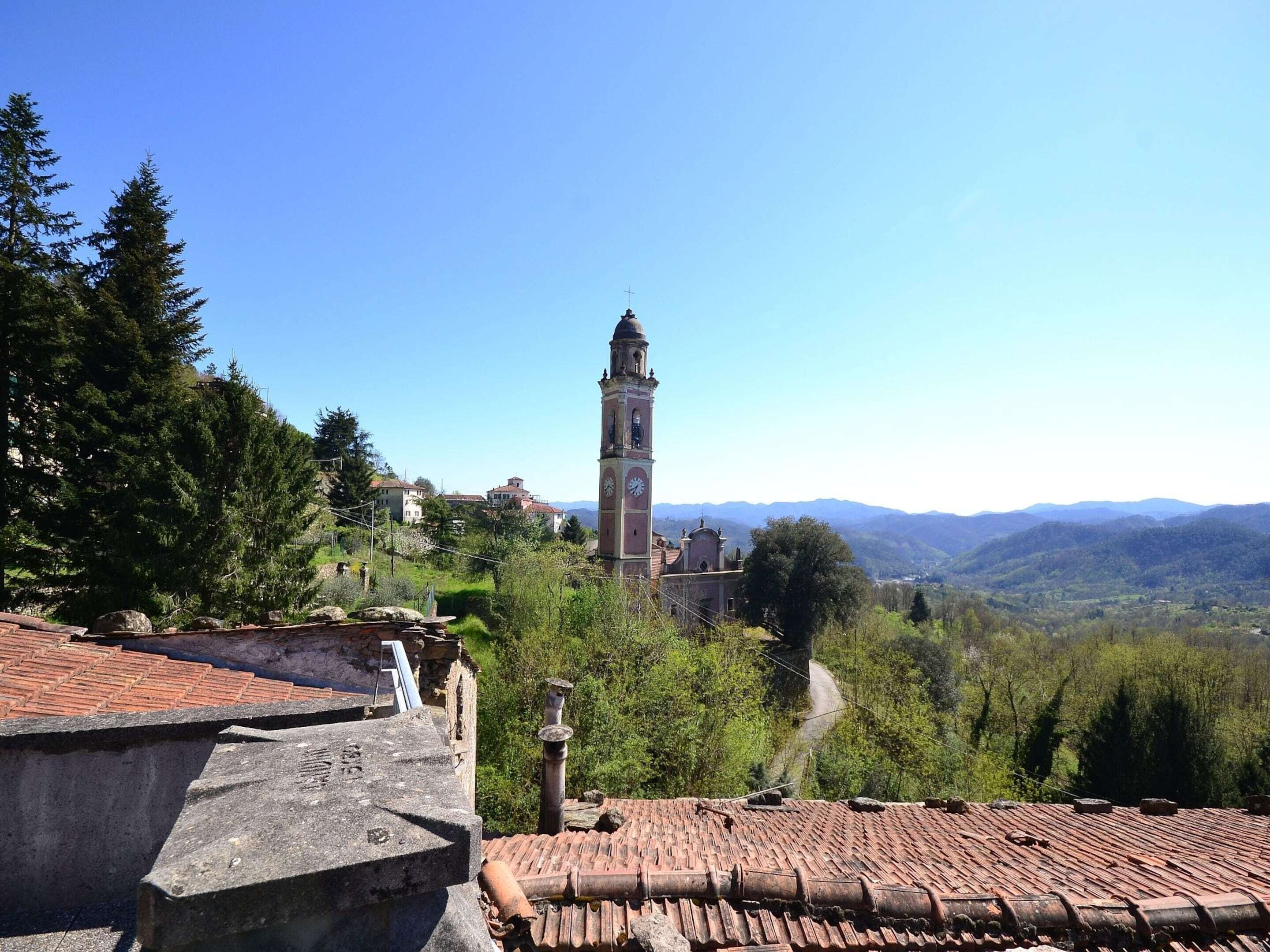 Une tour historique dotée d’une horloge, entourée d’une végétation luxuriante et avec des montagnes en arrière-plan.