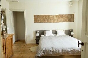 Une chambre à coucher comprenant un lit, des tables de chevet, une lampe fixée au mur, une armoire en bois et une porte donnant sur une autre pièce.