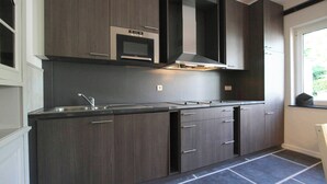 A modern kitchen with dark wood cabinets, a stainless steel sink, and a built-in oven. - Namur Mansion by the Meus (Hastiere)