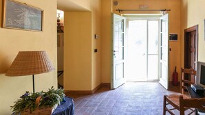 A hallway with a wooden ceiling, a door leading outside, a lamp, and a chair. - Belvilla by OYO Macetona - Suite (San Casciano dei Bagni)