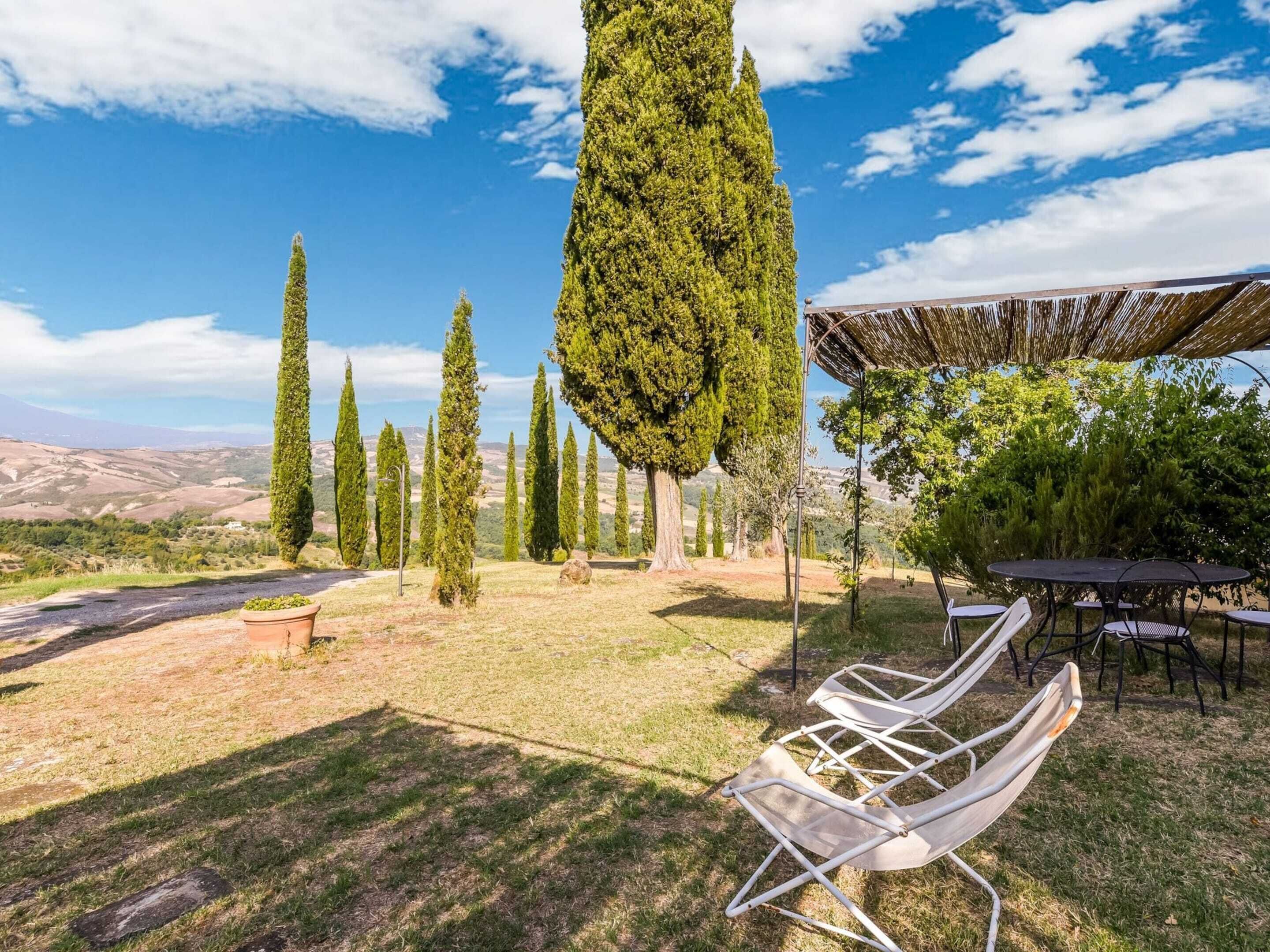 Um jardim com pérgola, área de estar ao ar livre e árvores altas.