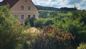Ein zweistöckiges Haus mit rotem Dach, umgeben von üppigem Grün und Hügeln im Hintergrund.