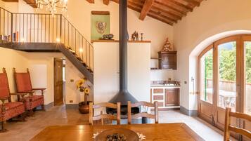 A spacious living area with a wooden staircase, a dining table with a decorative centerpiece, and a kitchen with wooden cabinets and a large window.