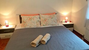 Una cama bien hecha con almohadillas florales, dos lámparas de noche y un cuadro en la pared.