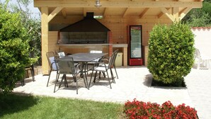 Un patio exterior con una pérgola de madera, una parrilla empotrada y un área de estar con sillas de metal.