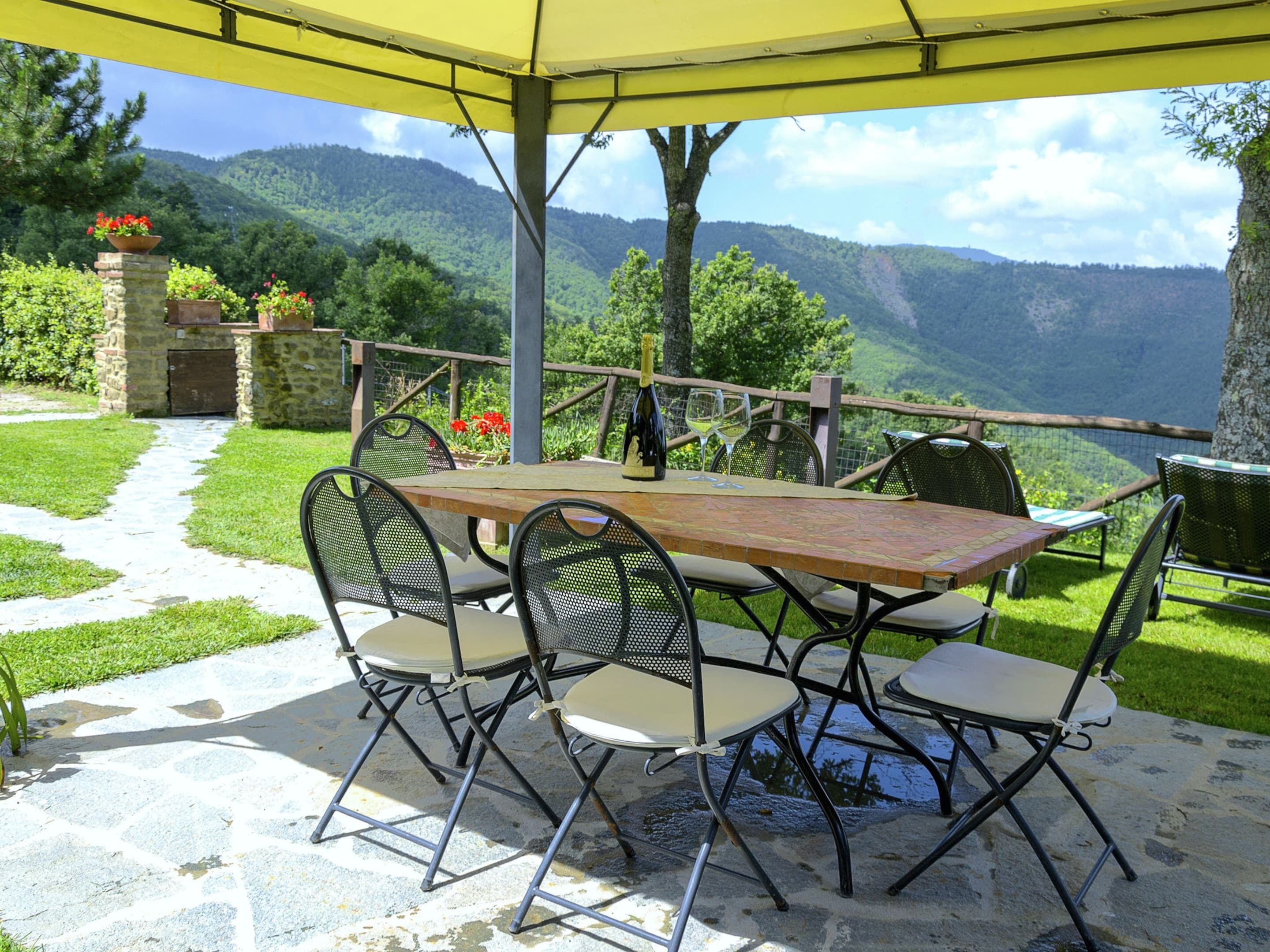 An outdoor patio with a table and chairs, a yellow umbrella, and a scenic mountain view.