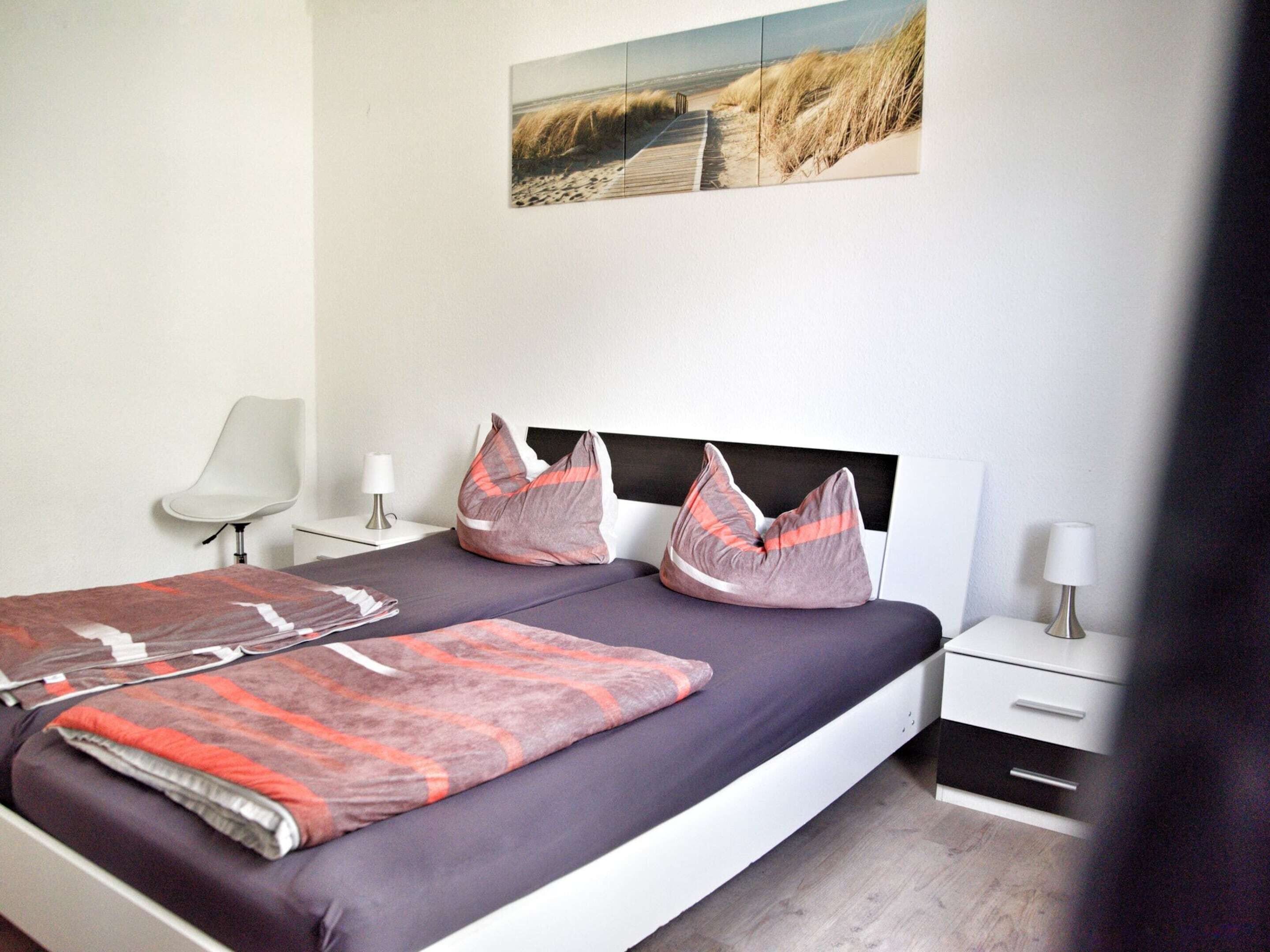 Une chambre à coucher moderne avec un lit, des tables de chevet, une chaise et un tableau accroché au mur.