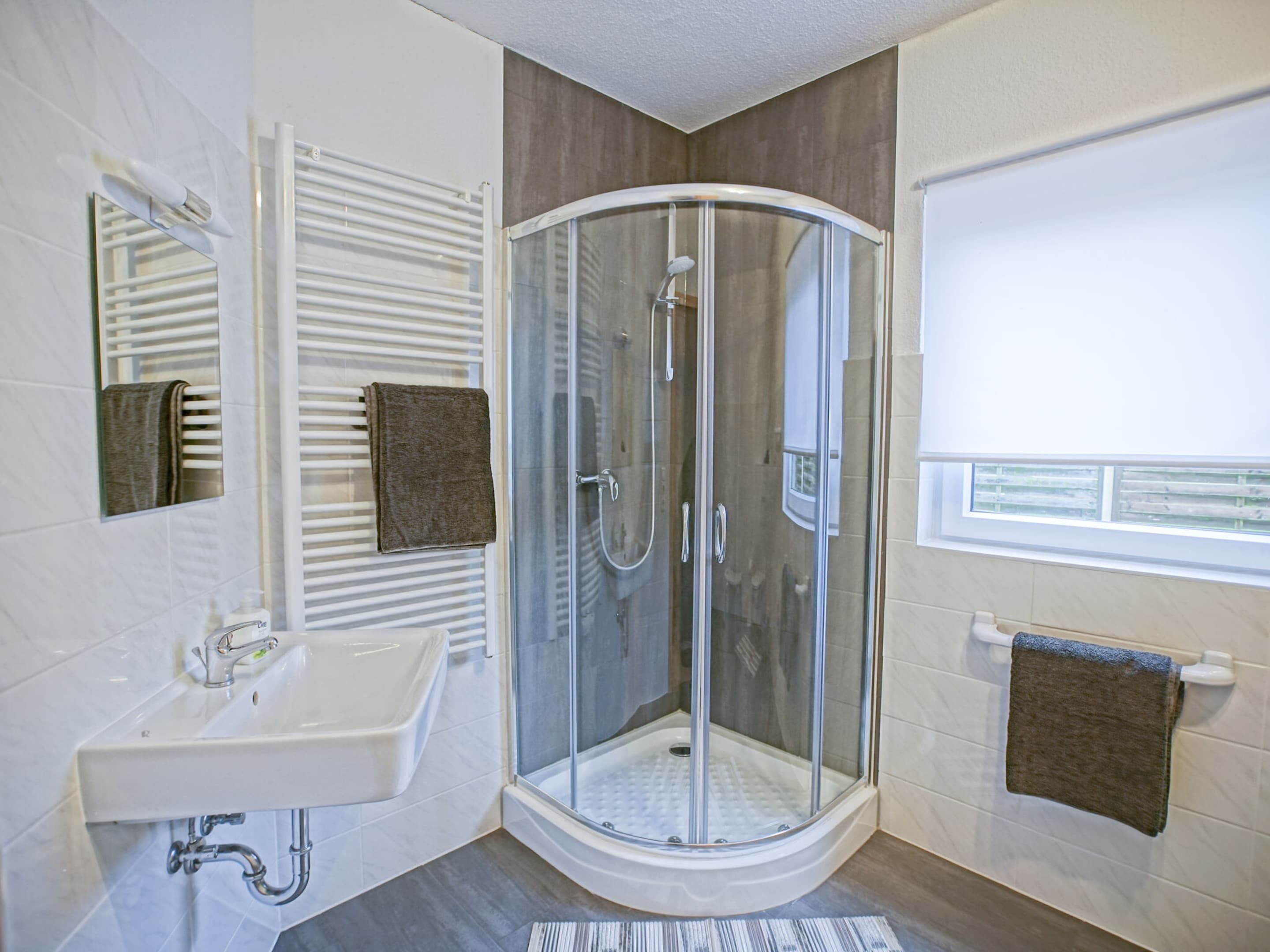 A modern bathroom with a glass-enclosed shower, a white sink, and a towel rack.