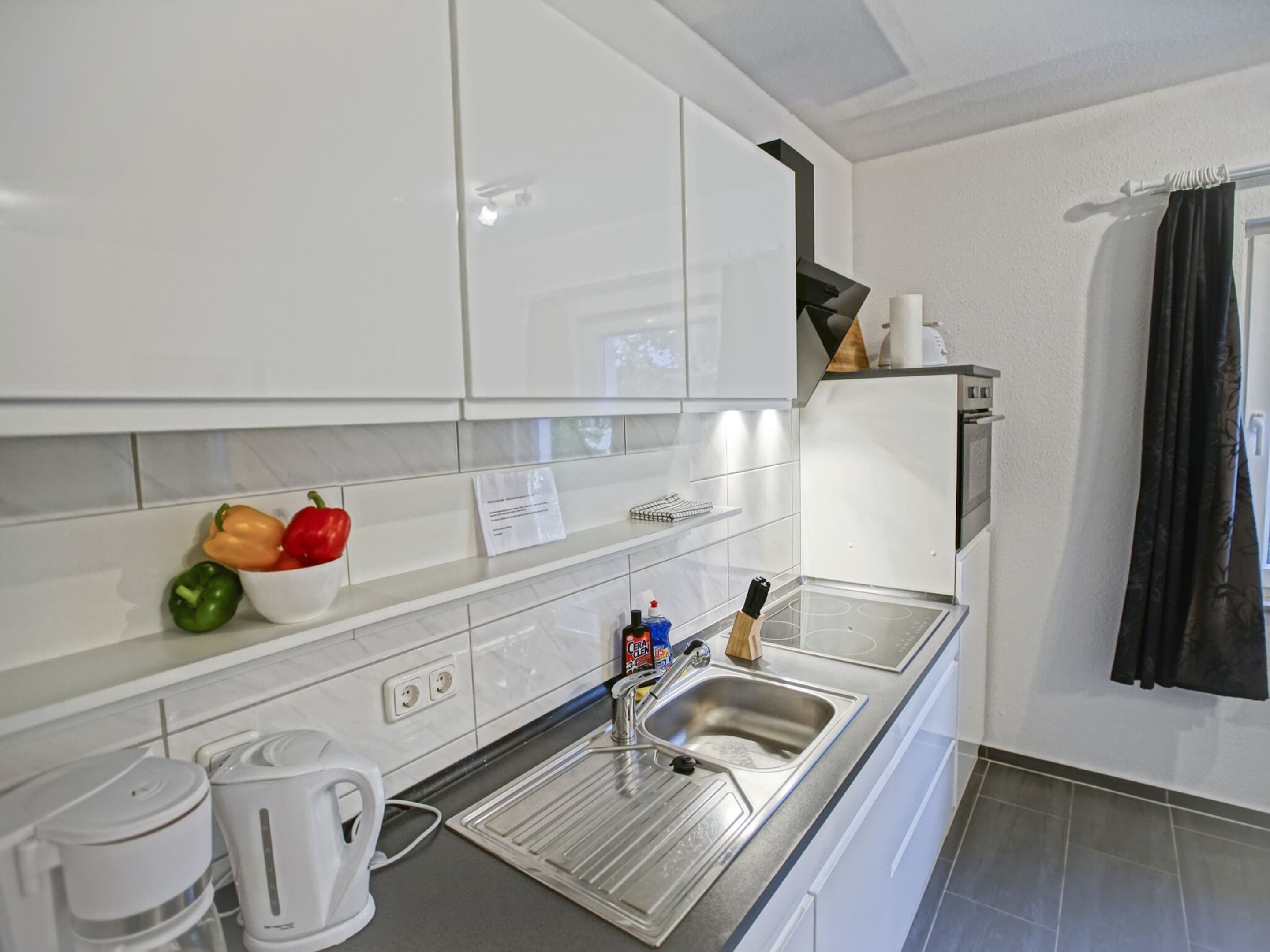 Een moderne keuken met witte kastjes, een roestvrijstalen spoelbak en een waterkoker.