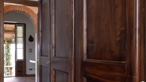 Una puerta de madera con manija de bronce, que da paso a una habitación con suelo de baldosas y un arco de ladrillo.