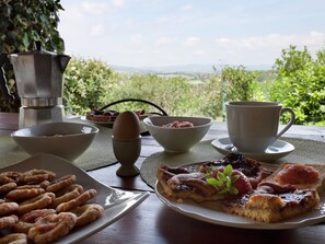 Une table de petit-déjeuner avec des croissants, une assiette de fruits, une tasse de café et une vue sur la campagne.