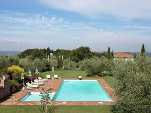 Une piscine rectangulaire bordée de briques, entourée d’une pelouse verdoyante et d’arbres.