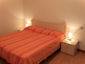 Ein Einzelbett mit orangefarbener, gestreifter Bettdecke, ein Nachttisch mit Lampe und eine Wandsteckdose.