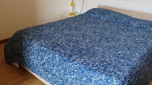 Een slaapkamer met een blauw bloemenbed, een witte nachtkastje met een gele lamp en een houten hoofdbord.