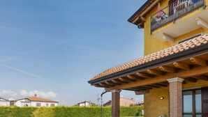 A two-story house with a covered patio, a swimming pool, and a well-maintained lawn. - Belvilla by OYO Casa Gialla A Due (Lazise)