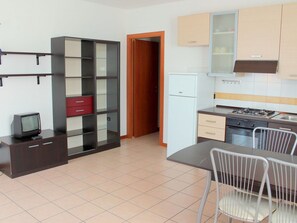 A compact kitchen with a refrigerator, stove, and dining area with chairs.
