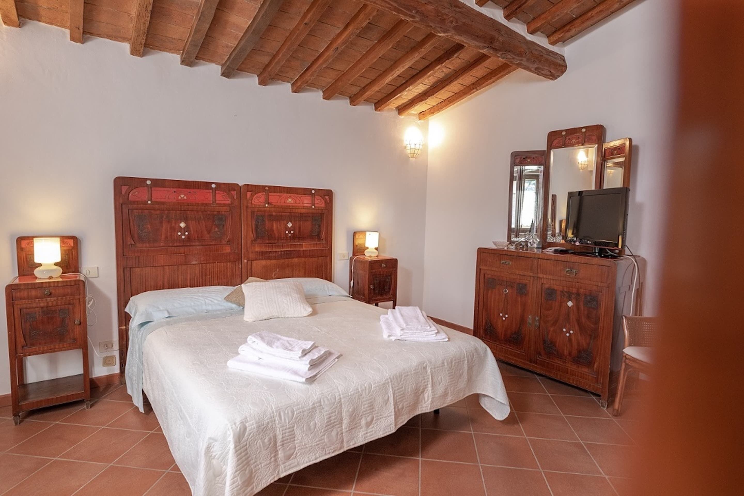 A bedroom with a wooden bed, bedside tables, a dresser, and a television.