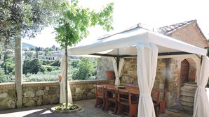 Eine Außenpatio mit Tisch und Stühlen unter einem weißen Baldachin, Steinmauern und Blick auf einen Hügel.