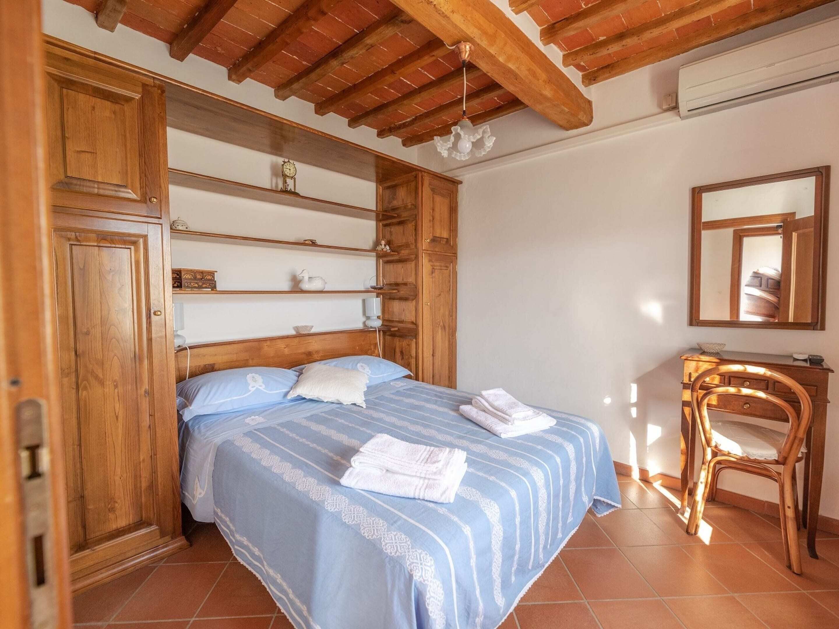 Een slaapkamer met een houten bed, een houten dressoir, een stoel en een spiegel aan de muur.