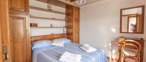 Een slaapkamer met een houten bed, een houten dressoir, een stoel en een spiegel aan de muur.