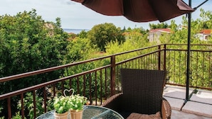 Ein Balkon mit Korbstuhl, Tisch und Topfpflanzen, sowie ein großer Sonnenschirm.