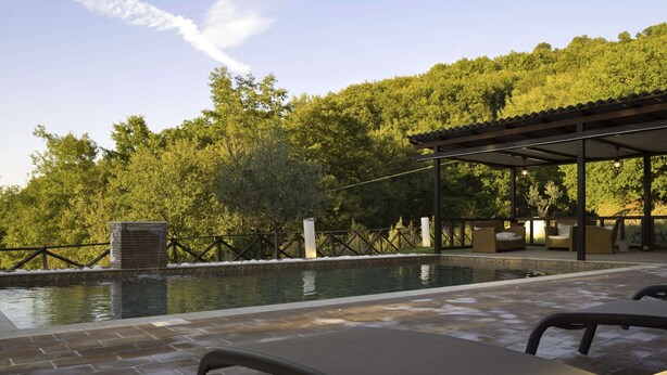 Un área de piscina con sillones de descanso, un espacio de estar techado y un muro de piedra.