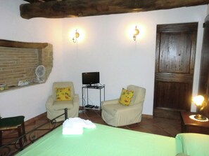 A room with two armchairs, a bed, a TV on a stand, and a wooden door. - Stay With Local Flavors (Piegaro)
