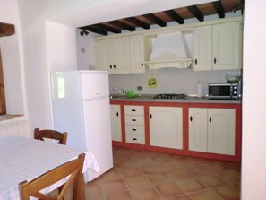 Une cuisine avec des meubles blancs, un réfrigérateur, un four à micro-ondes et une cuisinière à gaz.