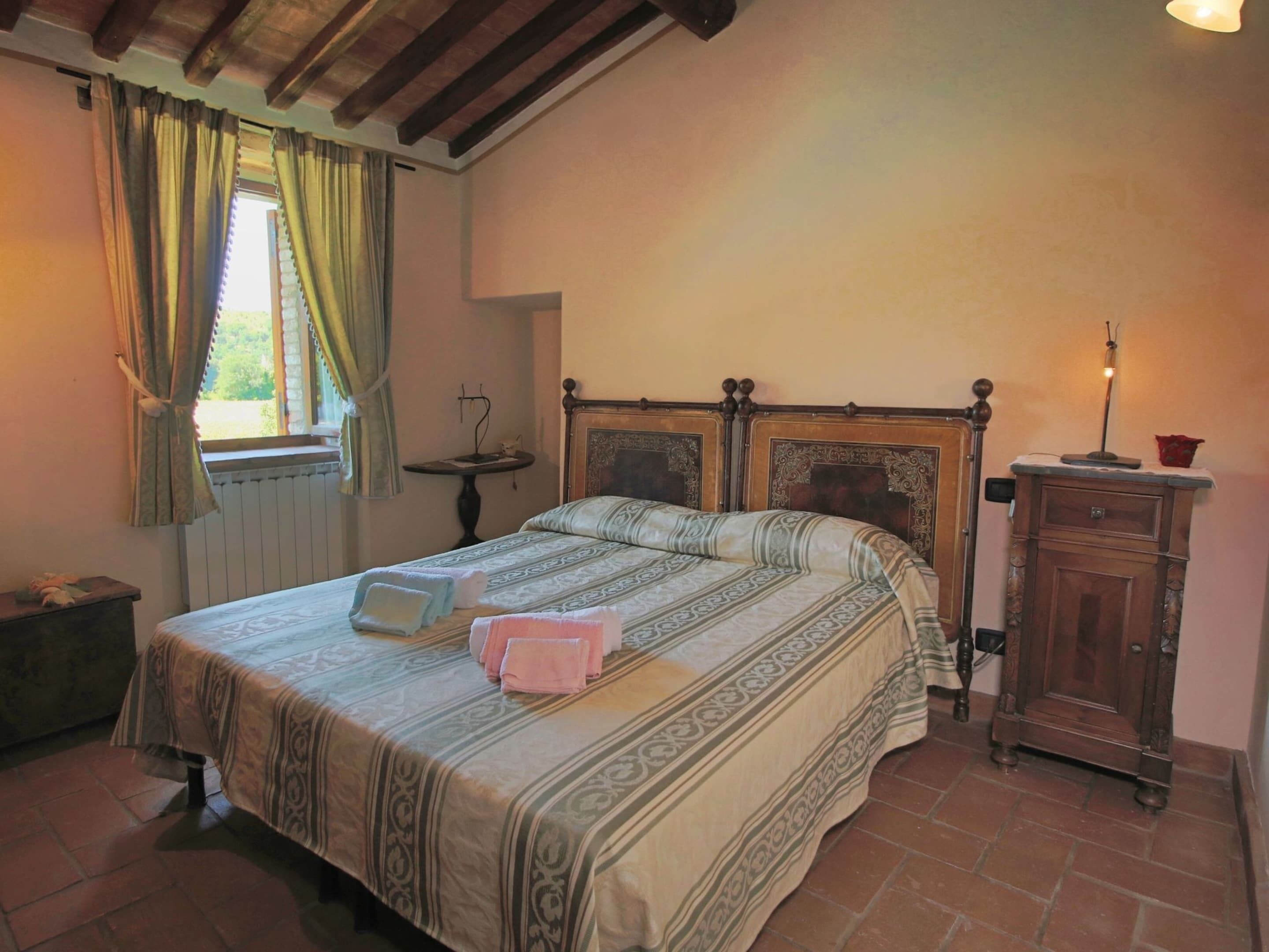 A bedroom with a bed, a nightstand, a dresser, a window with curtains, and a radiator.