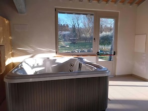 Une pièce dotée d’un jacuzzi, d’une grande fenêtre donnant sur des arbres et un bâtiment, et d’une porte avec une poignée.