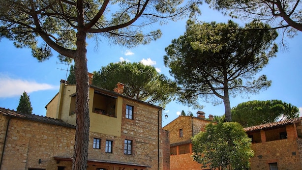 Un edificio de piedra con balcón, rodeado de árboles y un camino de grava.