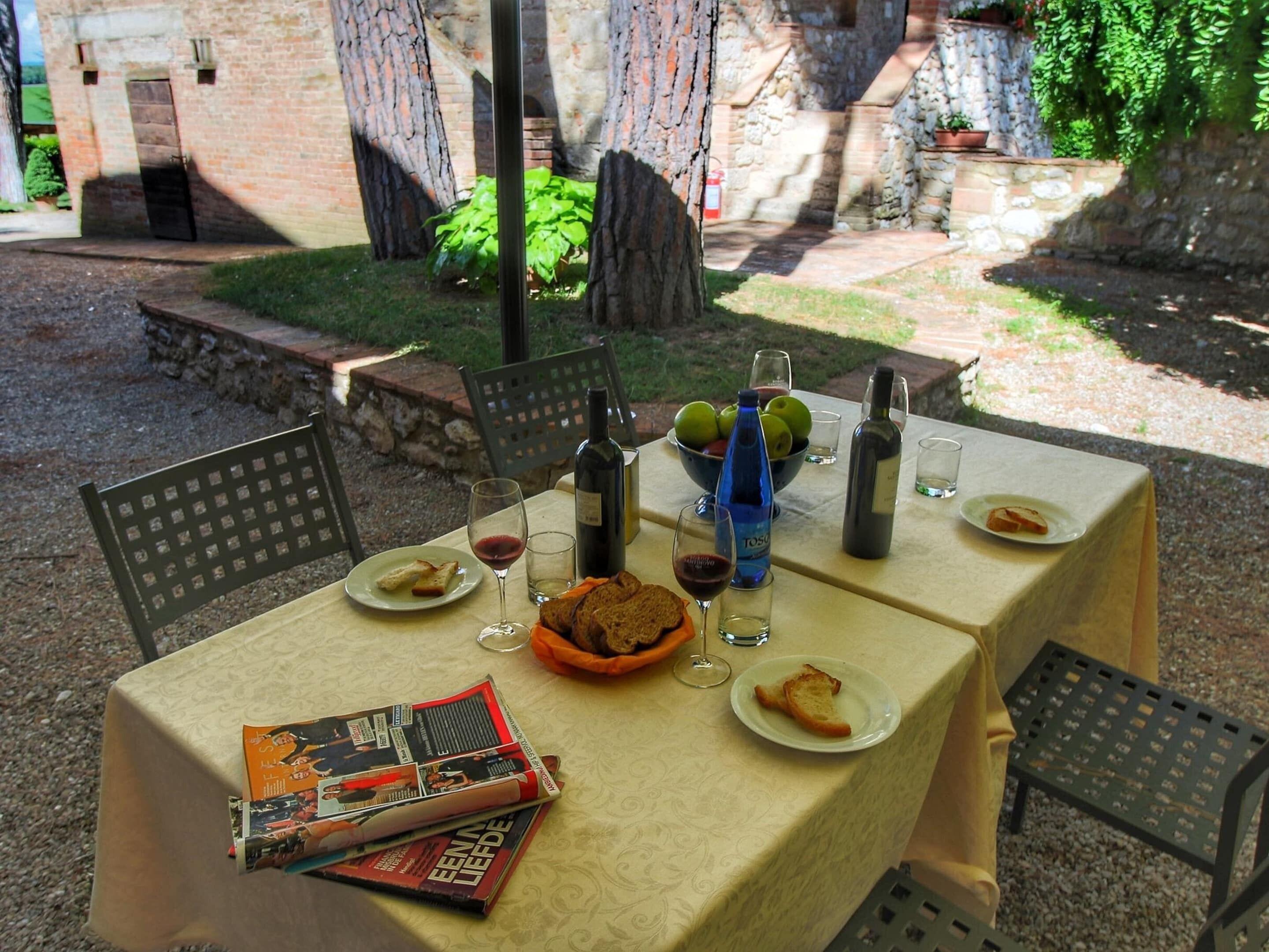 An outdoor dining table set up with a magazine, plates of food, glasses, and bottles.