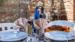 Mesa para dos personas, con platos, copas y una botella de vino, frente a un fondo de pared de piedra.