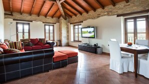 A spacious living area with a high wooden ceiling, a leather sofa with red cushions, a television, and a dining table with white chairs. - Magnificent old Country House With Garden and Private Pool, With Wifi (Salsomaggiore Terme)
