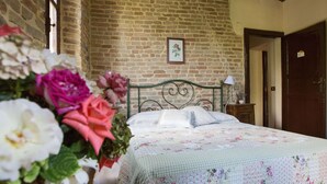 A bedroom with a brick wall, a bed with floral bedding, a picture on the wall, and a vase of flowers. - Magnificent old Country House With Garden and Private Pool, With Wifi (Salsomaggiore Terme)