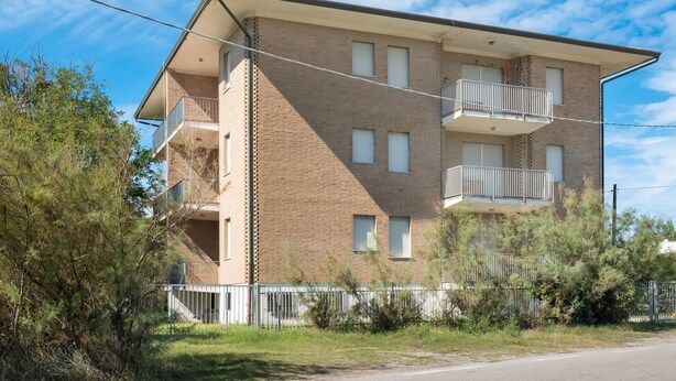 A multi-story apartment building with a brick facade, balconies, and a gated entrance. - Nice Holiday Home Close to sea Front, in Rosolina Mare, Near Venice (Rosolina)