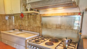 Una cocina con estufa a gas, lavamanos y campana extractora.