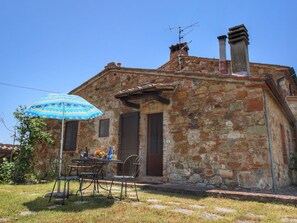 A stone building with a chimney, a door, and a table with chairs and an umbrella.