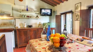 Una cocina con armarios de madera, un televisor montado en la pared y un frutero sobre la mesa.