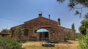 Una casa de piedra con un pequeño patio, una banca y una mesa con sillas.