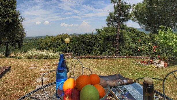 Una mesa con un frutero, una botella y un periódico.