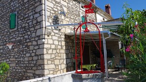Un edificio in pietra con un'insegna raffigurante un gallo rosso, un canestro da basket e tavoli all'aperto.