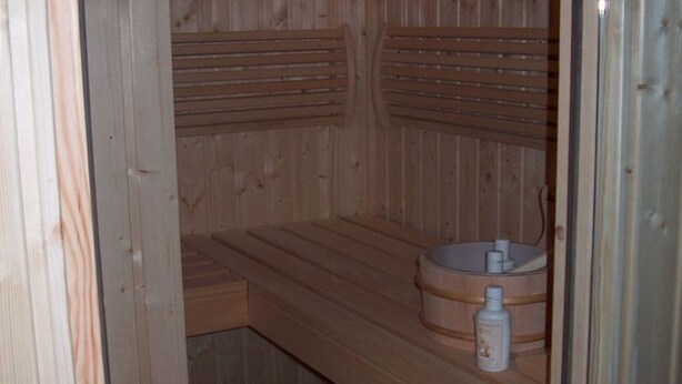 Eine Holzhütte als Sauna mit Bänken und einem Holzboden mit Spüle und Flasche.