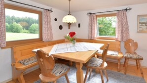 A dining area with a wooden table, benches, and chairs. There is a vase with flowers on the table. - Ferienhaus in Bayern mit Waldblick (Viechtach)